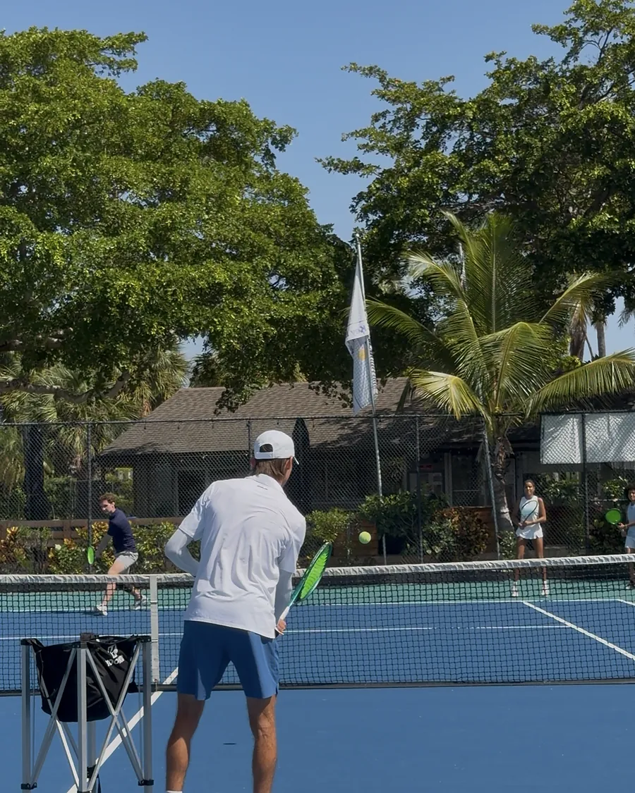 Coach feeding balls from a cart as players rally across the net