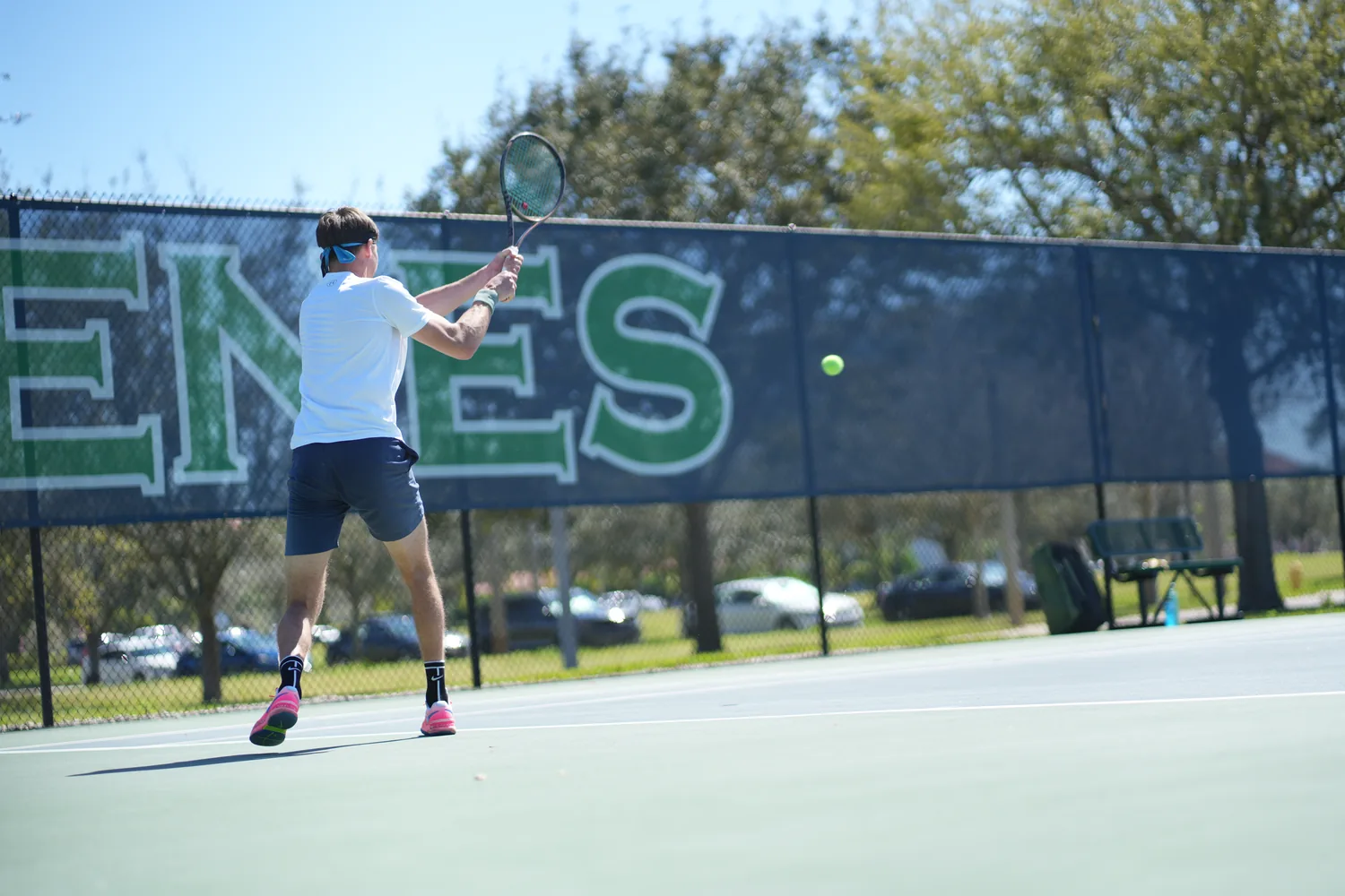 A competitive player striking a two-handed backhand at a college tennis facility in Florida